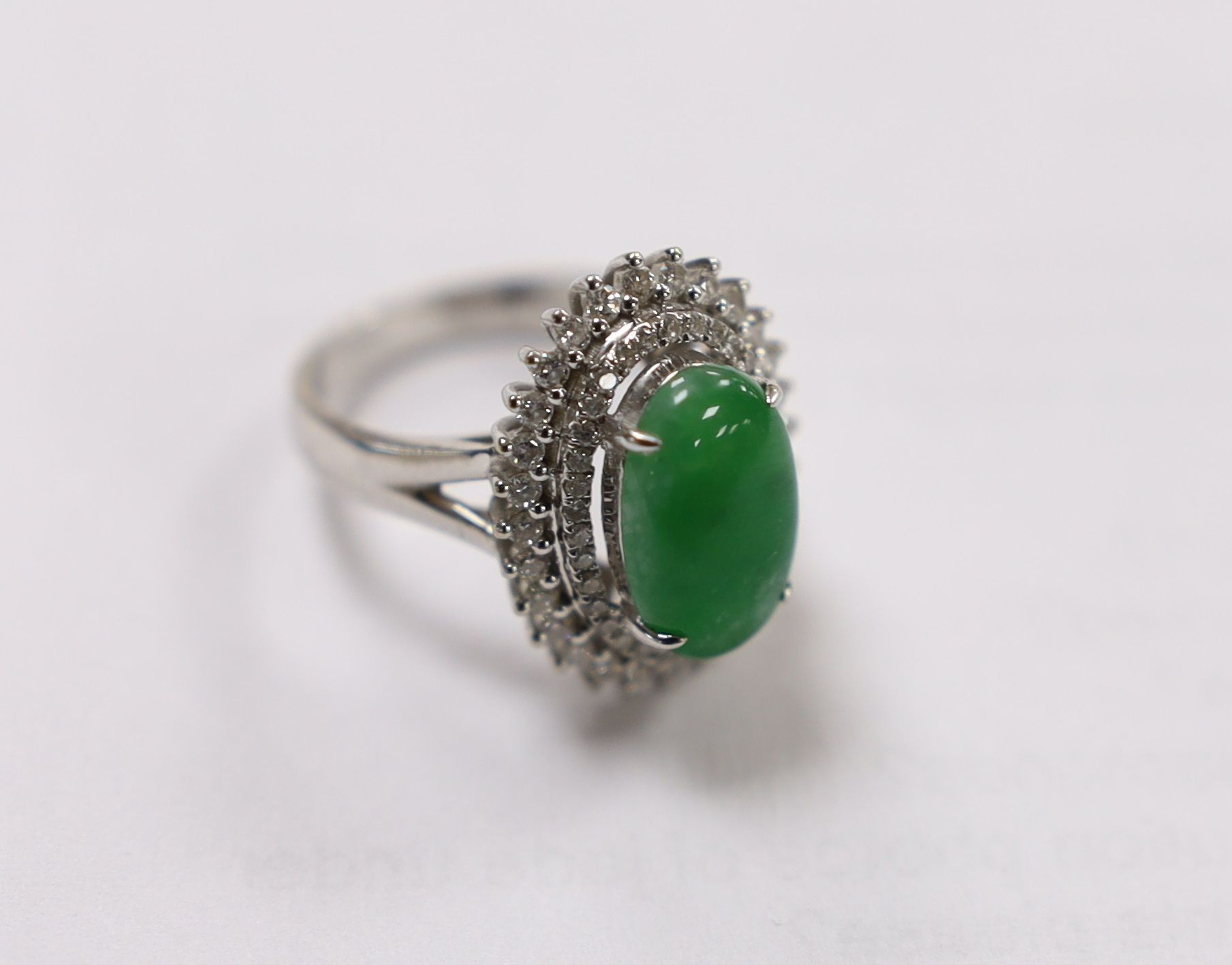 A modern 18k white metal, cabochon jade and two row diamond chip set oval cluster ring size L, gross weight 6.4 grams.